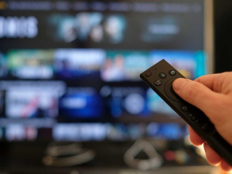 Tangan seseorang yang meemgang remote televisi saat sedang memilih tontonan