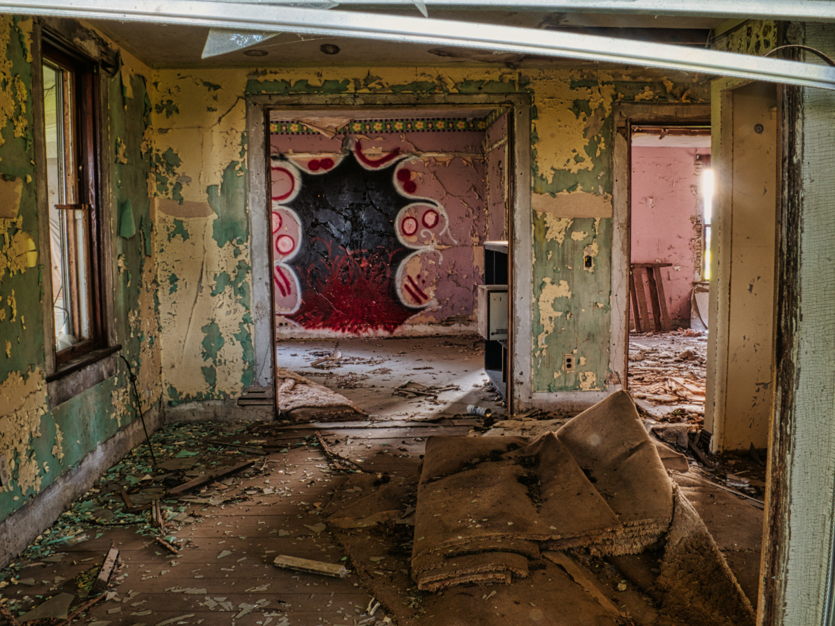 Bagian dalam bangunan kosong yang rusak dengan dinding mengeluupas dan lantai berantakan.
