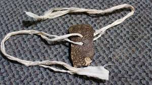 Benda yang disebut gasiang tangkurak, berbentuk seperti gasing kecil berwarna cokelat dengan tali putih yang digunakan untuk memutarnya, diletakkan di atas permukaan bertekstur abu-abu.